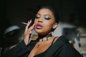Elegant woman with smoky eye makeup and pink nails holding a cigarette.