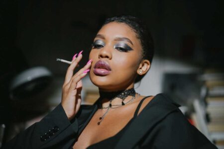 Elegant woman with smoky eye makeup and pink nails holding a cigarette.